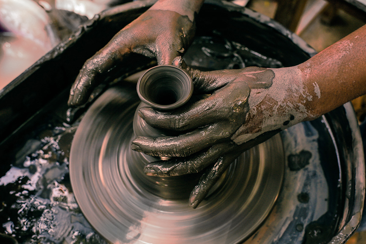 a potters hands and a pot on a wheel. The hands are covered in clay.